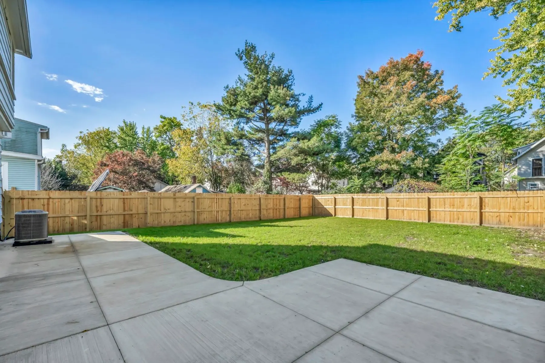Wide backyard lined by a new wood privacy fence and mature trees