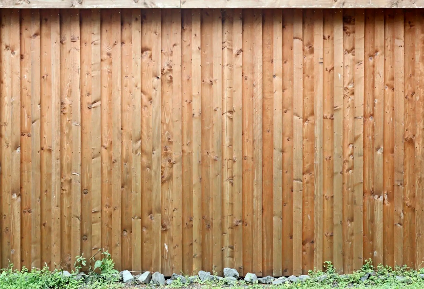 Board-on-board wood privacy fence along a gravel edge