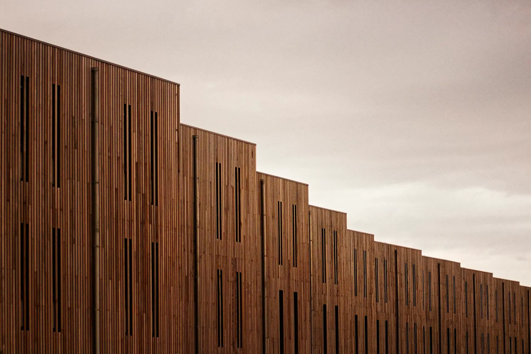 Stepped wall of vertical wood slats against an overcast sky
